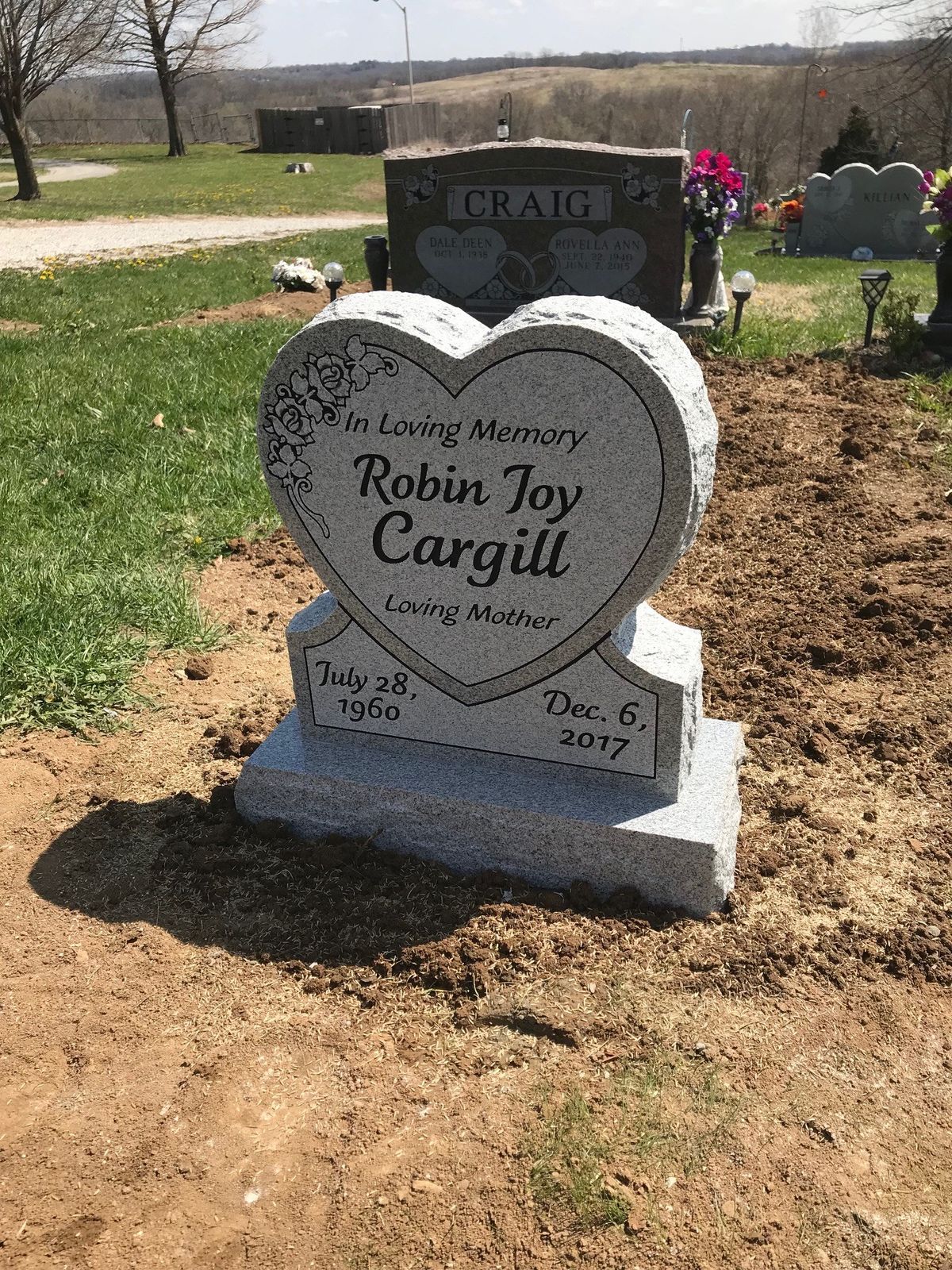 Heart shaped grey granite monument with a carved rose spray, on a two tier base