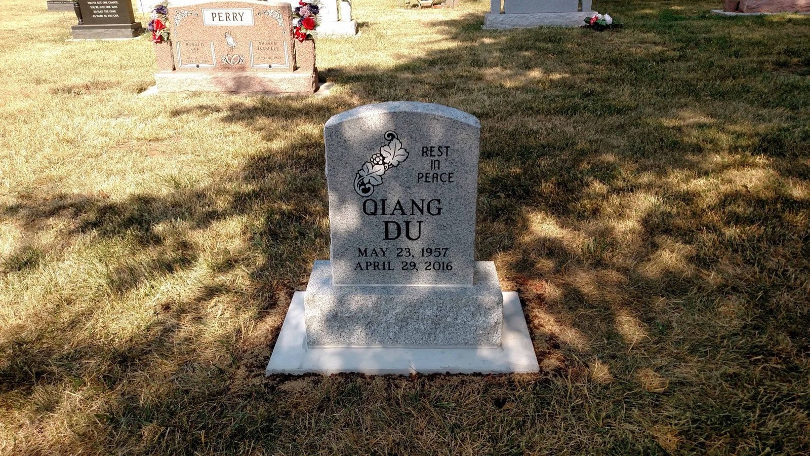 Grey granite upright monument with a carved rose and the words Rest In Peace, standing on a white granite base