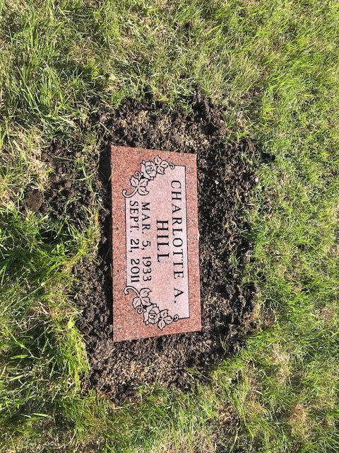 Mahogany granite flat grass marker with carved roses at the corners, freshly set into the ground